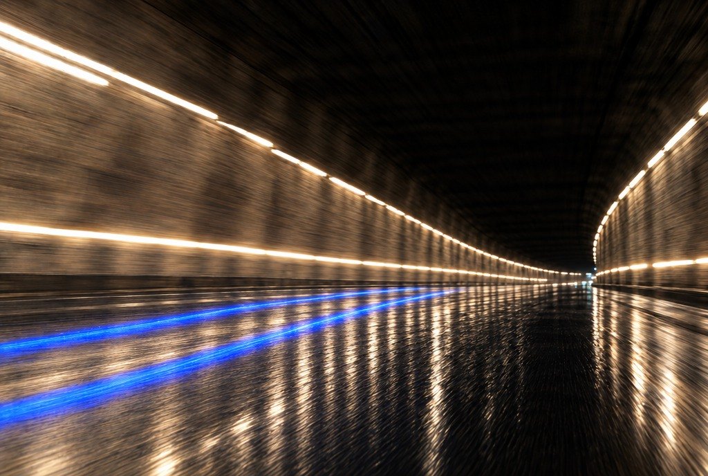 An empty tunnel under warm lights, a blue line running down the wet road